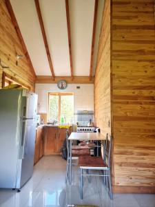 eine Küche mit Holzwänden, einem Tisch und einem Kühlschrank in der Unterkunft Refugio Wanglen Cabañas y Tinajas hidromasaje in Lago Ranco