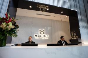two men in suits sitting at a counter in front of a merion sign at Meriton Suites Liverpool in Liverpool