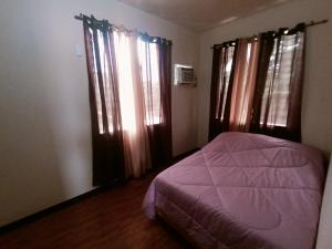 a bedroom with a bed with purple sheets and windows at Raymundo Residence in Dumaguete