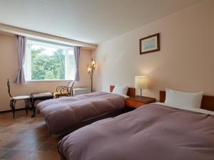 a hotel room with two beds and a window at Asama Kogen Hotel in Tsumagoi