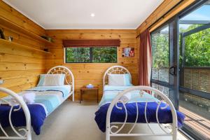 two beds in a room with wooden walls and windows at Ngongotaha Lakeside Lodge in Ngongotaha