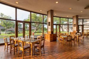 a dining room with tables and chairs and large windows at Hwange Safari Lodge in Dete