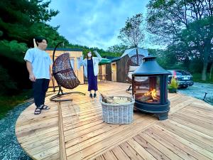 two people standing on a wooden deck with a fire pit at Fuji Dome Glamping in Fujikawaguchiko