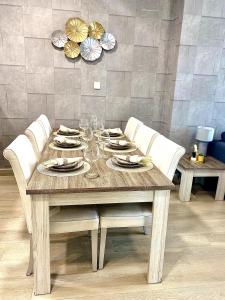 - une table en bois avec des chaises blanches, des assiettes et des verres à vin dans l'établissement Luxury 2BR for 6 with King Beds, Gym, Sauna in JVC, à Dubaï