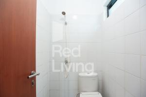 a bathroom with a toilet and a white tiled wall at RedLiving Apartemen EcoHome - DeLouvre Tower A Suginoki in Nalagat