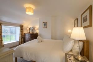 a bedroom with a white bed with a lamp and a window at April Cottage in Saint Just in Roseland