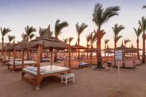 a beach with tables and umbrellas and palm trees at Pickalbatros Palace - Aqua Park Hurghada in Hurghada