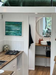 cocina con armarios blancos, lavabo y espejo en Little Pardalote Tiny Home Bruny Island, en Alonnah