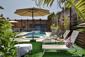 un patio con sillas, una sombrilla y una piscina en פנינת עוז - מתחם נופש יוקרתי, en Oshrat