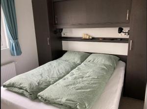 a bed with green comforter and pillows on it at Chalet 561 op Recreatiepark De Wielen in Sint Maarten +16 photos