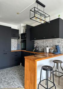 a kitchen with black cabinets and two bar stools at L'envolée - 15' de Paris & 10' du Stade de France in Saint-Denis