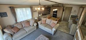 sala de estar con 2 sofás y cocina en Hot Tub Lodge Cornwall - Meadow Lakes Holiday Park en St Austell