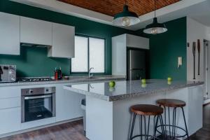 a kitchen with green walls and white cabinets and bar stools at AmazINN Places Penthouse en el corazon de La Condesa in Mexico City
