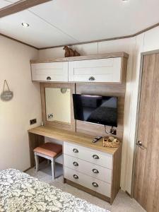 a bedroom with a dresser with a tv and a bed at Hot Tub Lodge Cornwall - Meadow Lakes Holiday Park in St Austell