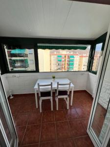 une table et des chaises blanches dans une chambre avec fenêtres dans l'établissement Apartman Los Cristianos-Cristimar, à Los Cristianos