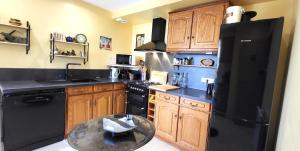 a kitchen with a black refrigerator and wooden cabinets at "La Colombe sous les Oliviers" Gîte jusqu'à 4 personnes - 75m2 - Sur Boooking - Rez de jardin Piscine Vue mer et lac in Spéracèdes