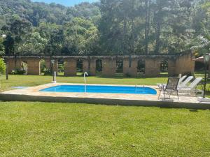 a swimming pool with two chairs and a house at Chalé Rio das Pedras in Santo Antônio do Pinhal