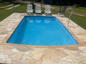 a swimming pool with two chairs and a table at Chalé Rio das Pedras in Santo Antônio do Pinhal