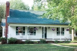 a white house with a porch with purple flowers at The Inn at Woodsong Acres in Conneaut