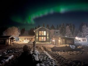 a person standing in front of a house under the aurora at Lägenhet med sjötomt. Vildmark i tätort. in Umeå