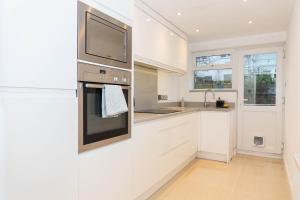 a kitchen with white cabinets and a tv on the wall at 2 Bed House-Great location in Cheltenham-Free WiFi in Cheltenham