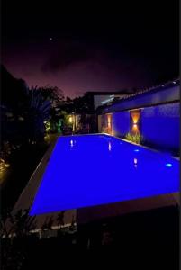 a blue swimming pool in front of a house at night at Cantinho da Cineka in Caraíva