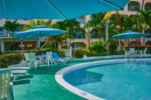 a swimming pool with blue umbrellas and chairs and tables at Sunbay Hotel in Christ Church