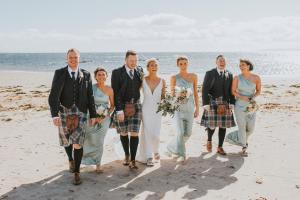 a bride and groom and their wedding party on the beach at The Waterside Hotel in Seamill