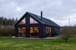 una casa negra con grandes ventanas en un campo en Vidunderlig fritidshus ved Skov og Golfbane en Skjern