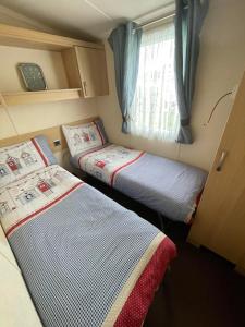 a small room with two beds and a window at Serendipity Caravan Hire in Chapel Saint Leonards