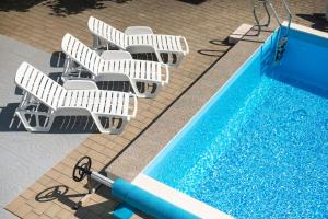 - une vue sur la piscine et ses chaises longues blanches dans l'établissement Apartments Denis, à Tribunj