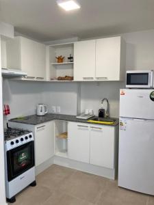eine Küche mit weißen Schränken, einem Herd und einem Kühlschrank in der Unterkunft Apartamento céntrico en Mercedes Uruguay in Mercedes
