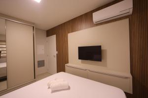 1 Schlafzimmer mit einem weißen Bett, einem TV und einem 6 x 6 cm großen Bett. in der Unterkunft Apartamento Espaço Aconchegante in Foz do Iguaçu