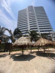 a tall building with palm trees and straw umbrellas at Espectacular Loft para estrenar, Reserva del Mar, playa salguero in Gaira