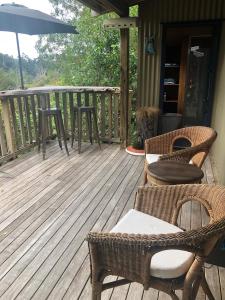 una terraza con sillas, mesas y sombrilla en Kākā Ridge Retreat Bush Hideaway en Tawharanui