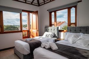 two beds in a room with large windows at HOTEL ALTIPLANO VILLA DE LEYVA in Villa de Leyva