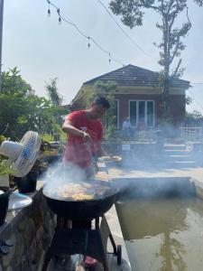 a man cooking food on a grill in front of a house at Villa Dikawah Ratu 1000m2 in Jabon