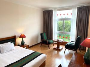 ein Hotelzimmer mit einem Bett, Stühlen und einem Fenster in der Unterkunft Dam San Hotel in Buon Ma Thuot