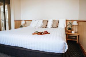 Una gran cama blanca con una bandeja de copas de vino. en Astor Inn, en Wagga Wagga