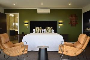 a bedroom with a white bed and two chairs at Atea Lodge in Coromandel Town