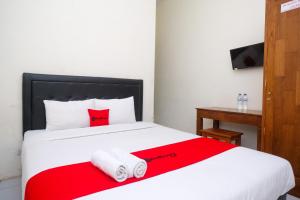1 dormitorio con 1 cama roja y blanca y toallas en RedDoorz Syariah at Griya Hanum Condoongcatur en Kejayan