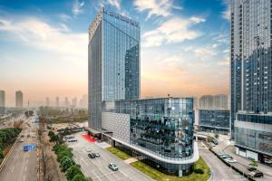 ein hohes Glasgebäude mitten in einer Stadt in der Unterkunft Hampton by Hilton Wuhan High-Speed Railway Station in Qingshan