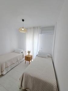 a white bedroom with two beds and a table at Dúplex 8, en primera línea de playa in Sanlúcar de Barrameda