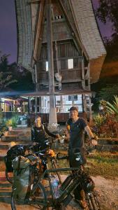 dos hombres parados junto a sus bicicletas delante de una casa en NUANSA HOMESTAY Authentic&Hospitality, en Rantepao