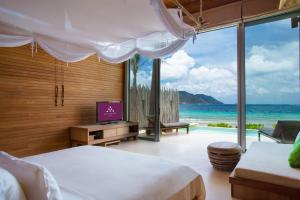 a bedroom with a bed and a television and the ocean at Six Senses Con Dao - Turtle Island Paradise in Con Dao
