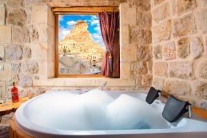 a bath tub in a stone bathroom with a window at Cappadocia Pema Cave Hotel in Ortahisar