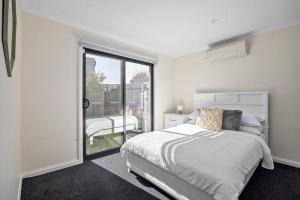 a white bedroom with a bed and a sliding glass door at Coastal Stroll at Safety Beach in Safety Beach