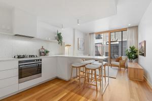 una cocina con armarios blancos y taburetes de bar en Stylish 2-bed Victorian Terrace in Carlton, en Melbourne