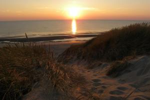 einen Sonnenuntergang über einem Strand mit Meer und einem Sandweg in der Unterkunft Ammophila 1 in Egmond aan Zee