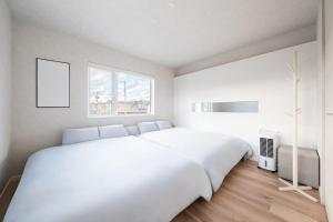 a white bedroom with a large white bed and a window at THE Prestige in Asahikawa